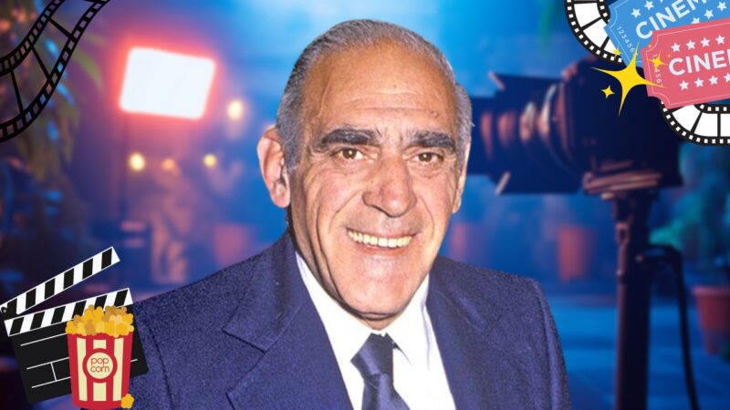 Abe Vigoda, smiling while wearing a suit and tie. The background features a blurred film set with cameras and lighting, along with decorative elements like film strips and popcorn containers, emphasizing a cinematic theme