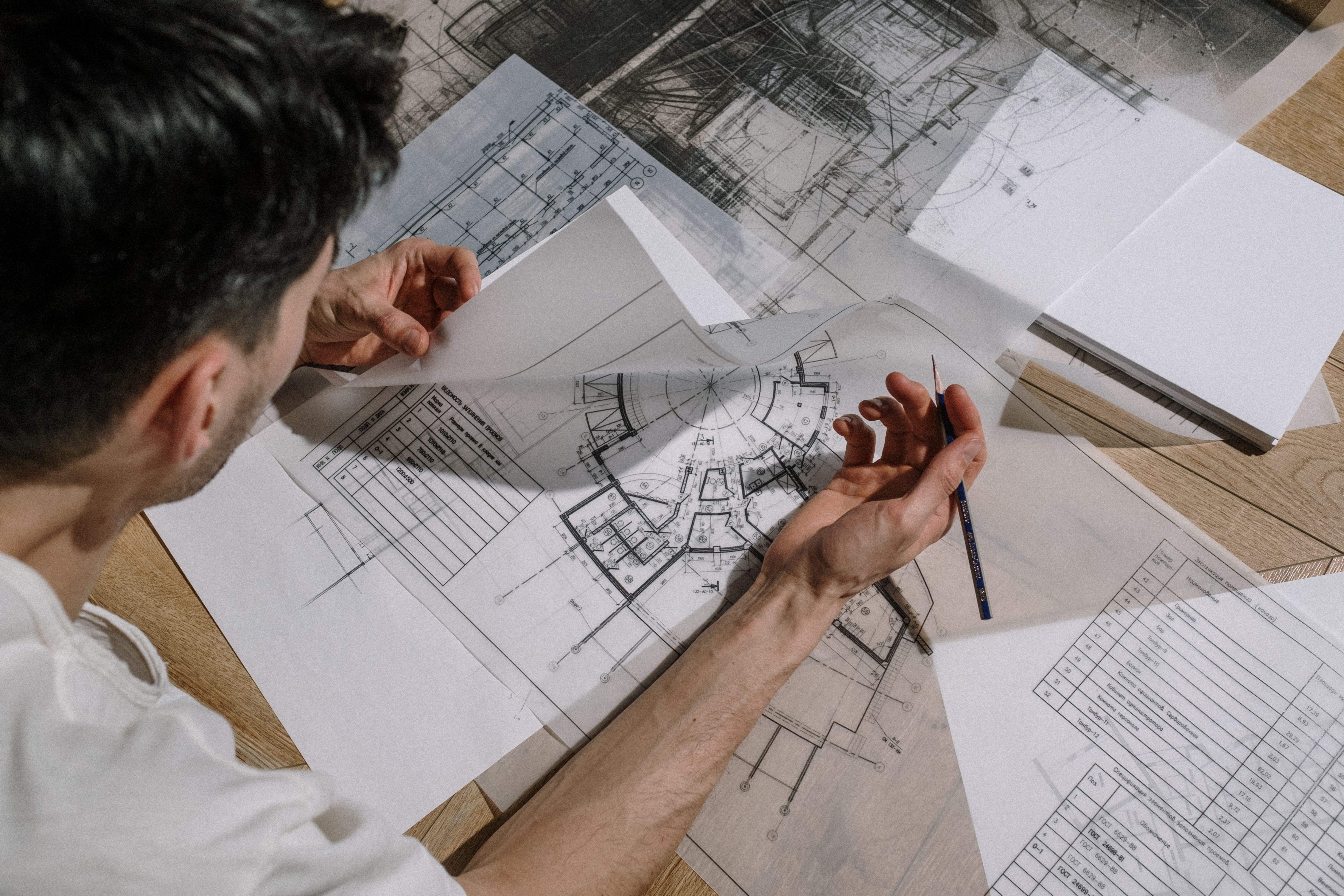 Architect studying and sketching over detailed architectural blueprints indoors