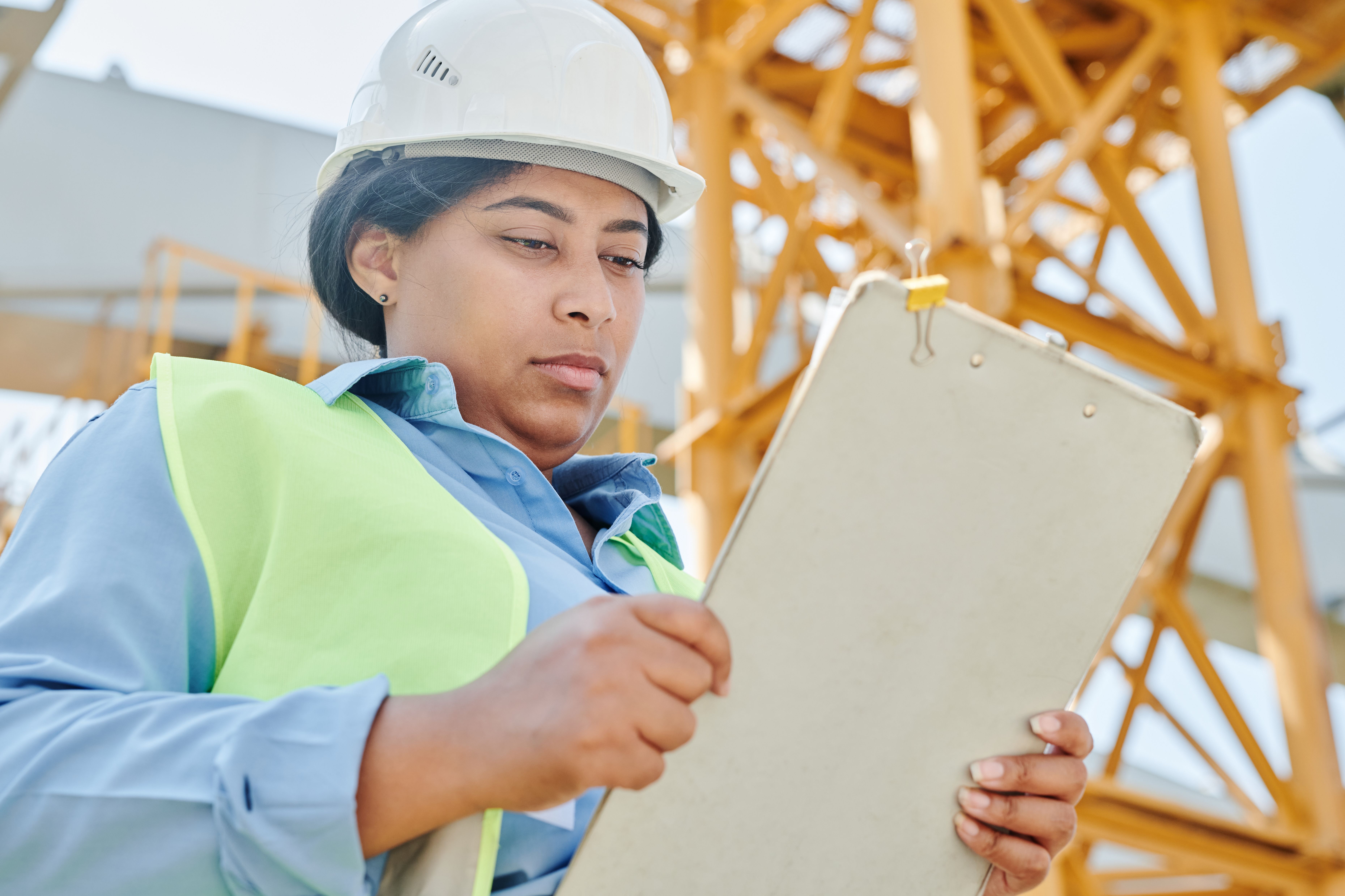 Female construction worker with clipboard and helmet inspecting a building site