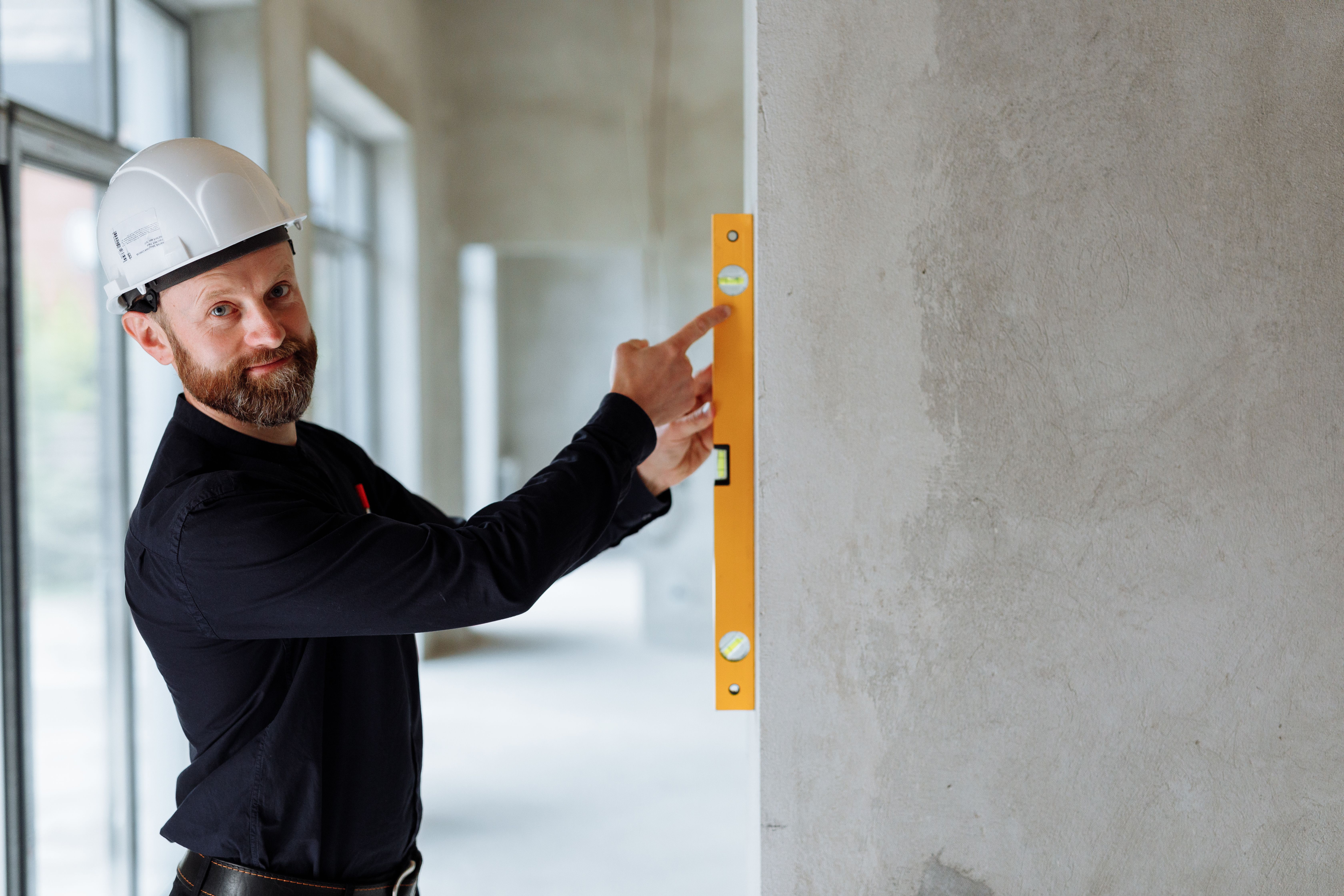 Engineer in a hard hat using a spirit level on a wall at a construction site
